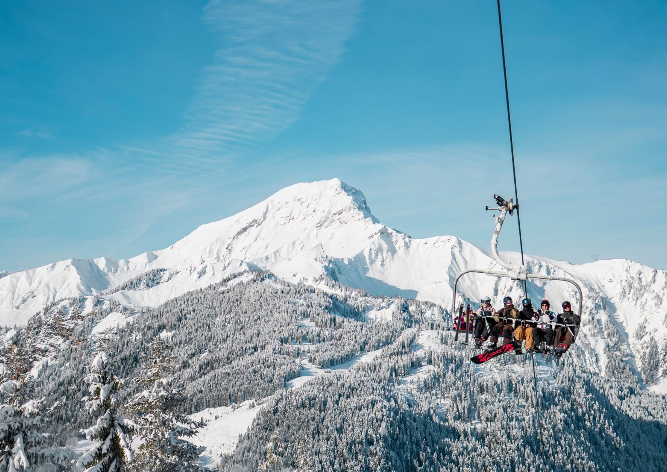 Skiers on a chairlift above Chatel with snow-covered Portes du Soleil mountains in the background