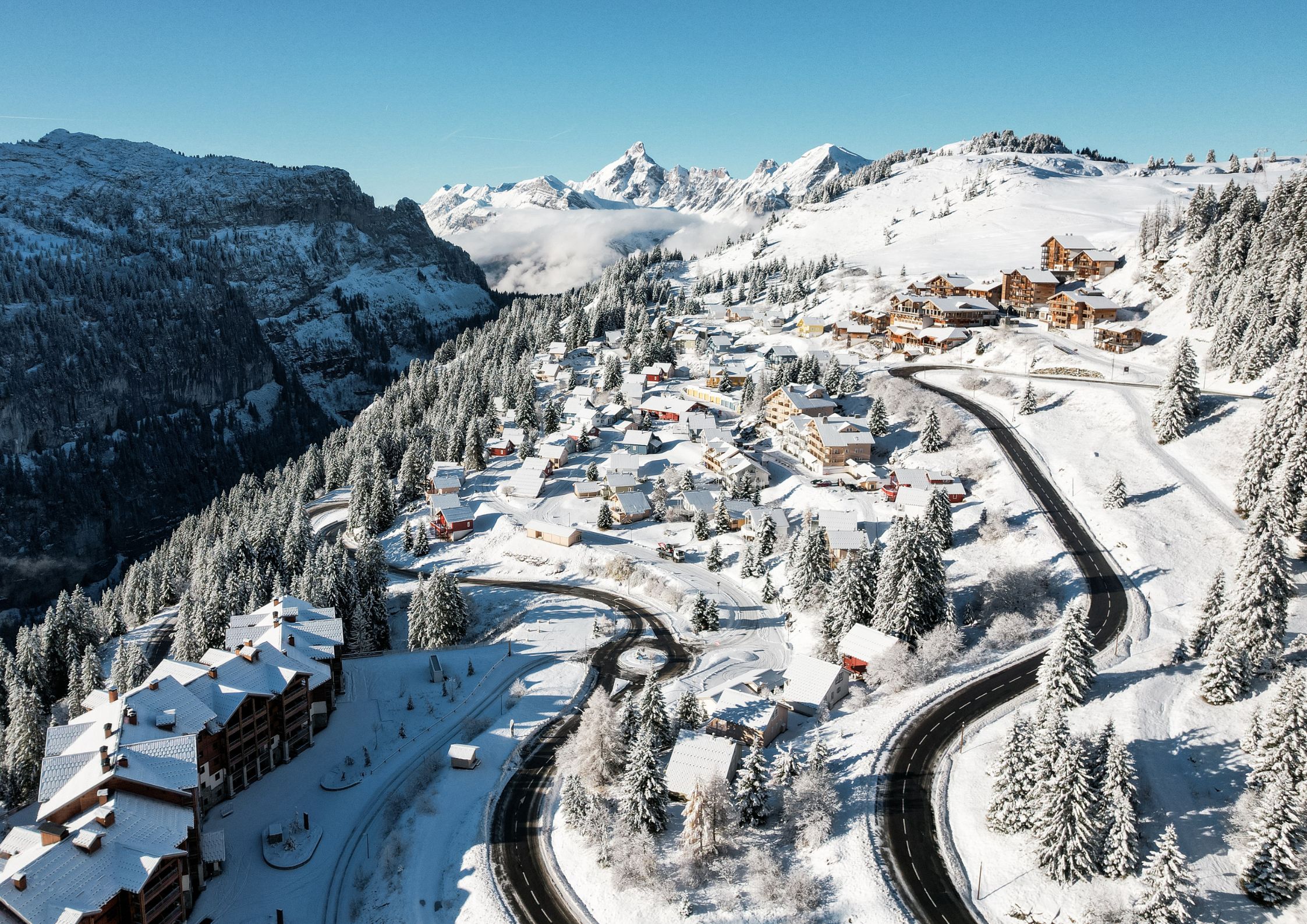 Aerial view of Les Carroz village on the road to Flaine with snow-covered chalets and Grand Massif peaks behind