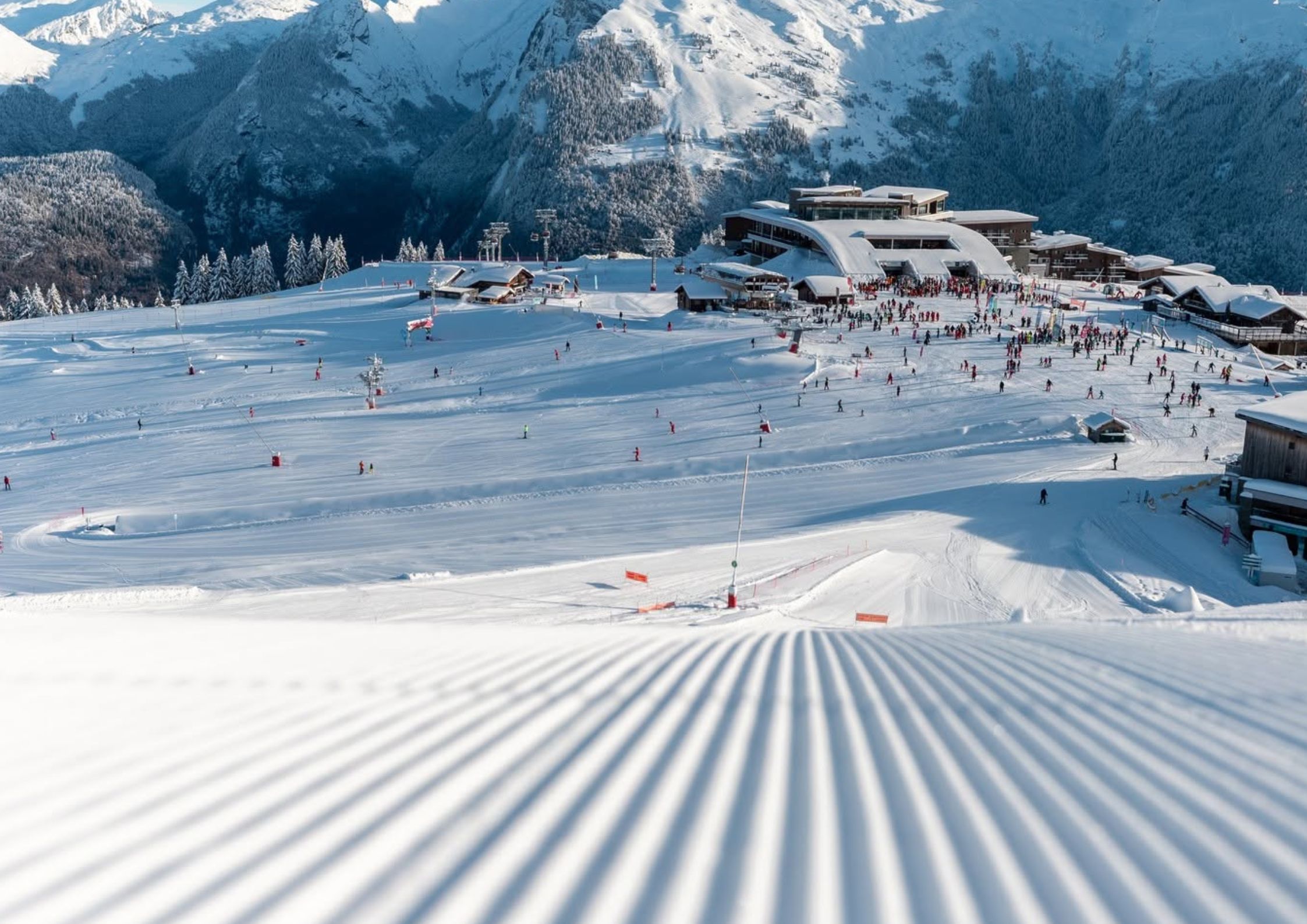 View from freshly groomed corduroy ski run looking towards the Samoëns 1600 ski station and the Grand Massif Express arrival area with skiers on the slopes.